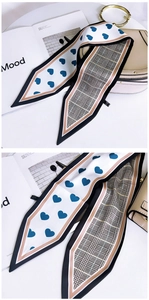 Detail of silk scarf with heart print and plaid patterns tied on a beige handbag handle