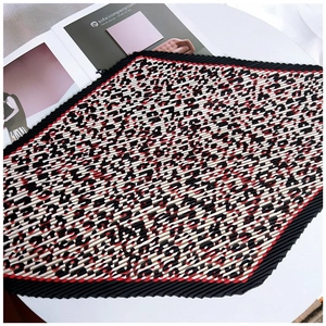 Close-up of pleated silk scarf with bold leopard print and red accents on white surface