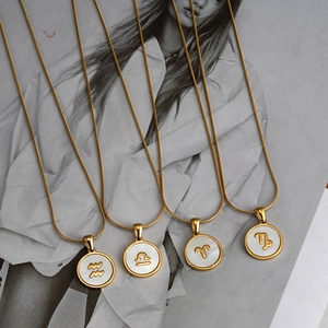 Macro view of four 18K gold-plated stainless steel zodiac shell necklaces on a magazine