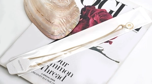 Detail view of gold stainless steel necklace with letter B pendant on a white shell base