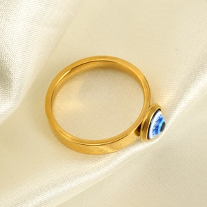 Macro shot of gold stainless steel ring with blue resin evil eye on white silk