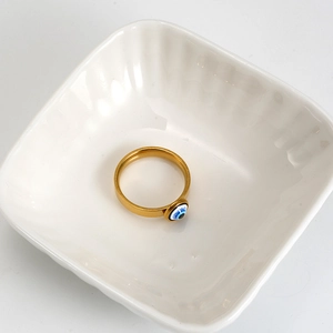Close-up of 18K gold stainless steel ring with blue resin evil eye inlay on white ceramic