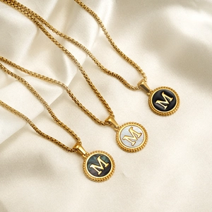 Detailed macro view of 18K gold letter M pendants with black, white, and green enamel finishes