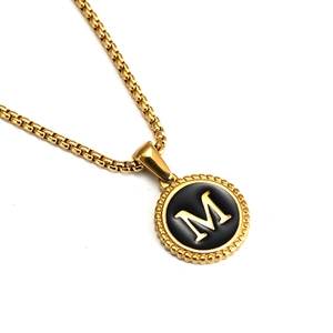 Macro detail of 18K gold-plated box chain with black enamel round pendant and letter M