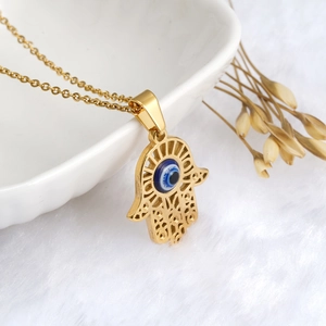 Gouden Hamsa hand ketting met blauwe boze oog hanger op een witte pluche basis
