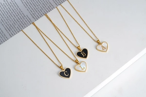 Detail of four heart-shaped gold necklaces with black and white initial shell pendants