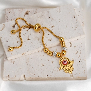 Adjustable 18K gold Hamsa hand bracelet with red evil eye charm on white marble