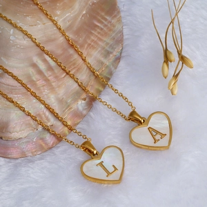 Golden heart shell necklace with initial letters A and L on white plush background