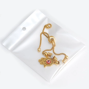 Detail of 18K gold Hamsa Hand bracelet with red Evil Eye charm in PE packaging