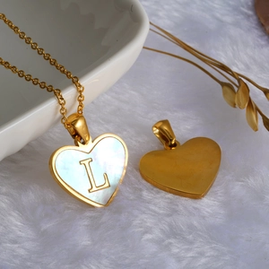 Detail view of heart-shaped shell pendant with golden letter L on white faux fur