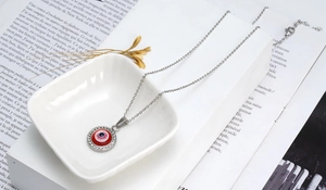Détail du collier argenté avec pendentif œil maléfique rouge et cristaux pavés sur assiette