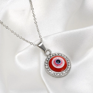 Détail macro du collier en acier avec pendentif œil bleu sur fond rouge et cristaux