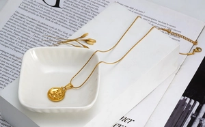 Detailed shot of gold Scorpio coin necklace on a white ceramic bowl with snake chain link