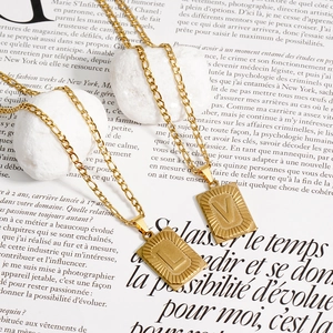 Détail de pendentifs rectangulaires dorés avec lettres L et V sur chaînes Figaro