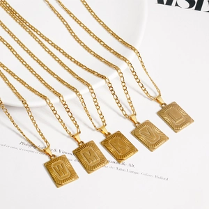 Gros plan de pendentifs rectangulaires dorés avec lettres sur des chaînes Figaro