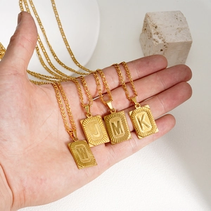 Détails de pendentifs carrés dorés W J M K sur chaînes Figaro tenus dans la main