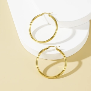 Elegant gold hoop earrings with mirror finish displayed on white circular pedestals