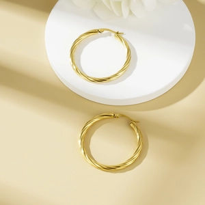 Chunky gold twisted hoop earrings with textured spiral design for women in a studio setting