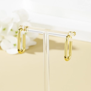 Polished gold U-shaped geometric hoop earrings displayed on a minimalist acrylic stand