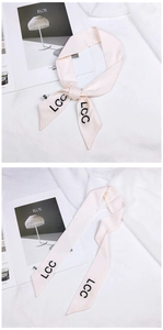 Detail of light pink silk ribbon scarf with bold LCC letters tied in a bow on magazine