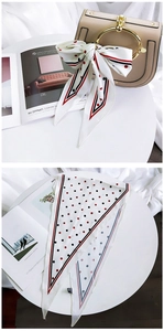Close-up of a white silk scarf with red and black polka dots used as a handbag accessory