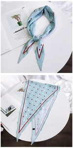 Detail of light blue silk scarf with red dots and striped edges on a white table