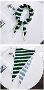 Detail of green and navy striped twilly silk scarf tied in a bow on a magazine