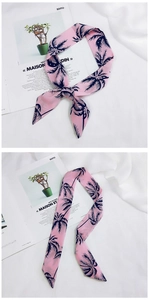 Detailed close-up of a pink silk scarf with navy palm tree prints on a minimal background
