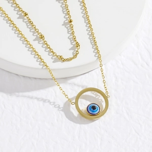 Macro view of gold anklet with small beads and blue evil eye charm on white pedestal