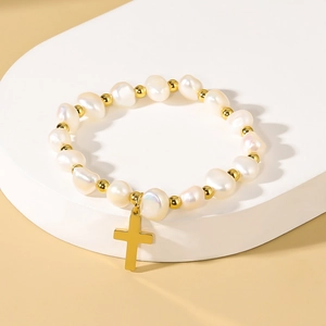 Baroque freshwater pearl bracelet with gold cross pendant on a minimalist display stand