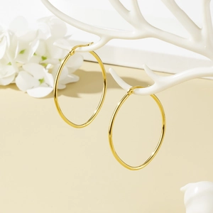 Elegant gold Mobius hoop earrings for women hanging on a white jewelry stand with flowers