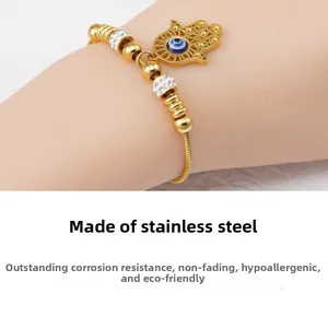 Macro detail of golden Hamsa Hand and Evil Eye charms on stainless steel snake chain