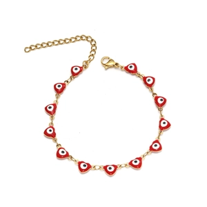 Détail du bracelet doré avec breloques cœurs rouges, motif œil protecteur et fermoir mousqueton