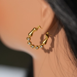 Détail d'une boucle d'oreille cœur en acier doré 18k avec cristaux sur modèle