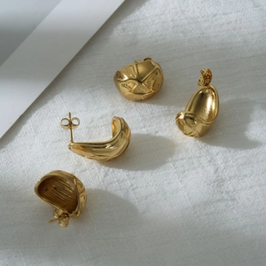 Golden irregular pea earrings with textured geometric design on white linen