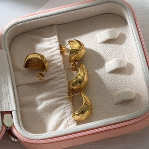 Close-up of golden geometric and crescent stud earrings inside a pink jewelry box