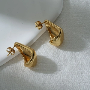 Détail de boucles d'oreilles dorées irrégulières sur un socle blanc minimaliste