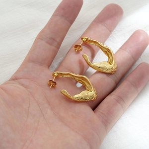 Irregular lava-style 18K gold earrings with organic twisted design held by hand
