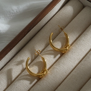 Dettaglio degli orecchini a C in oro 18K con un elegante design a nodo intrecciato