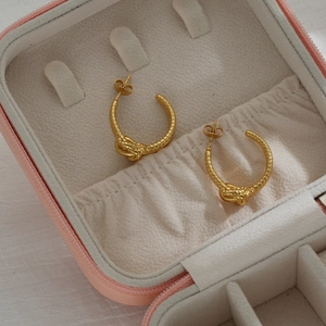 Orecchini a cerchio a C intrecciati placcati oro 18K su portagioie in velluto beige