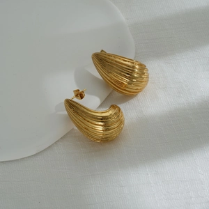 Detail of gold waterdrop earrings with textured stripes on white aesthetic display