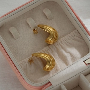 Chunky gold striped teardrop hoop earrings on beige velvet jewelry box lining