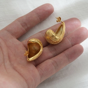 Detailed close-up of golden teardrop earrings featuring fine vertical striped texture