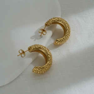 Close-up of gold C-shaped earrings with intricate pineapple texture and butterfly clasp