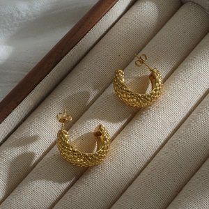 Macro shot of 18K gold-plated C-shaped earrings with vintage quilted texture in jewelry box