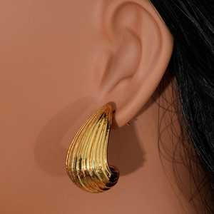 Golden chunky teardrop earrings with vertical ribbed texture on female model
