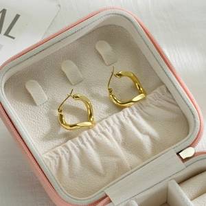 Detailed close-up of golden twisted geometric hoop earrings on soft velvet in a gift box