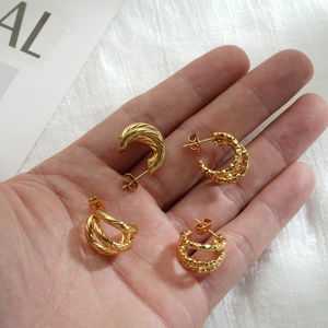 Detail of 18k gold plated C-shape twisted and faceted hoop earrings on a hand