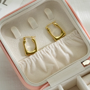 Detailed macro of gold-plated U-shaped earrings in a light pink velvet jewelry box