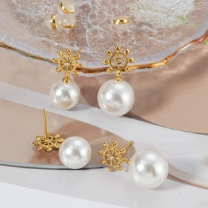 Detail view of gold helm pearl earrings with zircon inlay on a textured glass tray